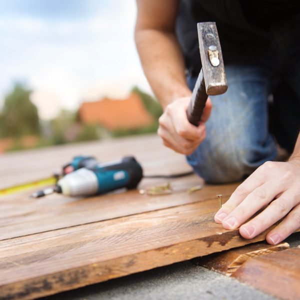 Handyman installing wooden flooring in patio, working with hammer